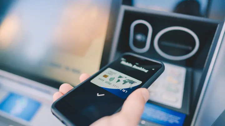 Person holding a cellphone with card information in front of an ATM
