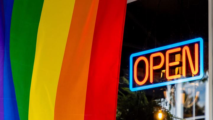 Open sign at a shop with the original rainbow flag in front